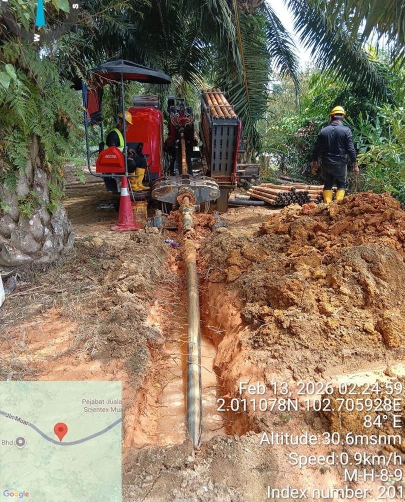 CASE excavator digging trench in palm oil plantation, black corrugated duct visible in trench. Jln Muar, Bukit Bakri, Johor (8 June 2026).