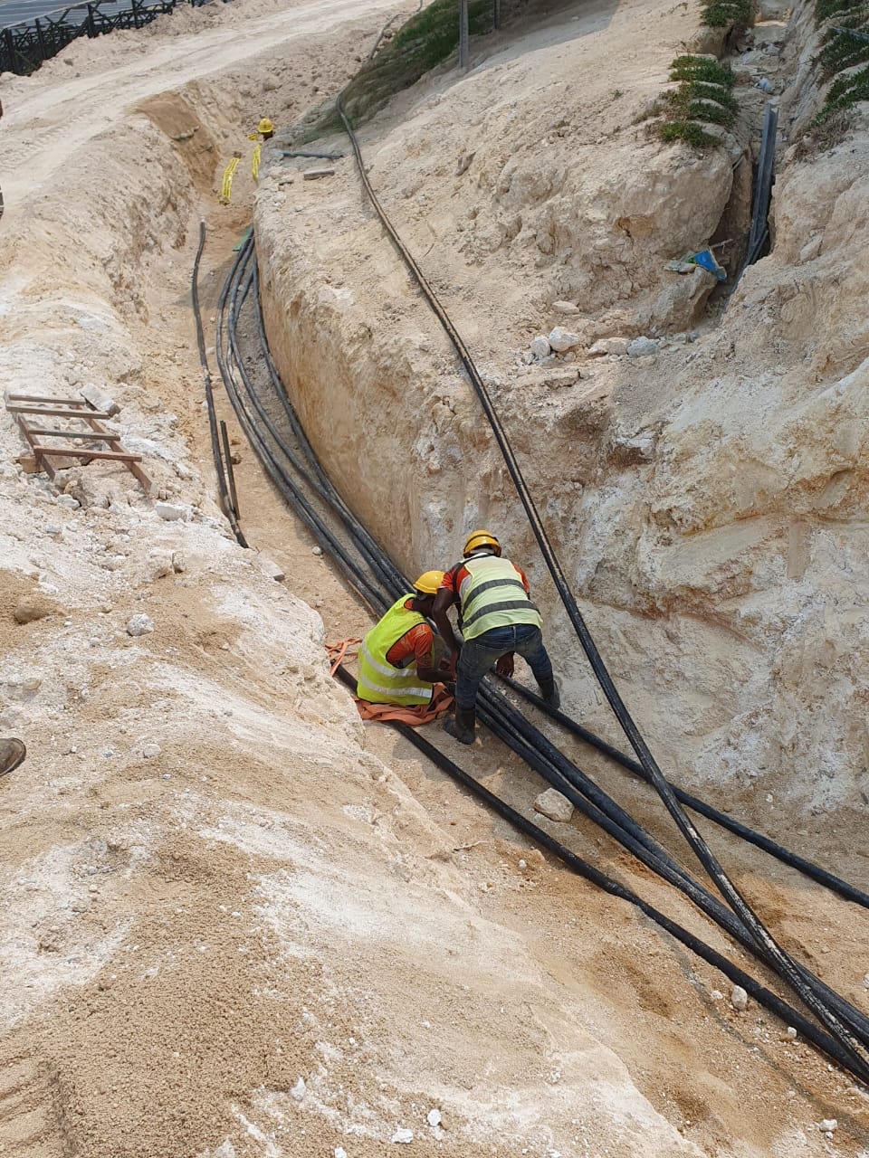 Workers managing cable bundles in a deep trench cut into the hillside at the solar farm.